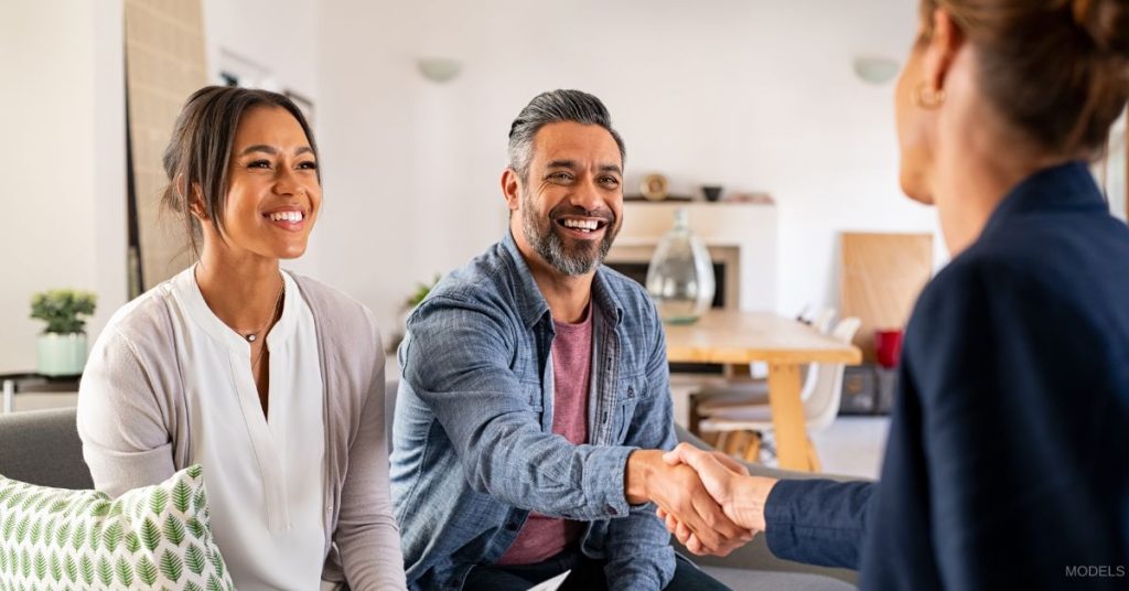 A couple smiling while having a consultation with a woman. (Models)